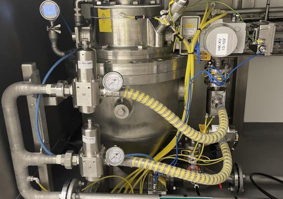 Vista frontal de un componente de transferencia neumática de acero inoxidable, con manómetros, reguladores y tubos flexibles amarillos para el transporte de polvos o gránulos.