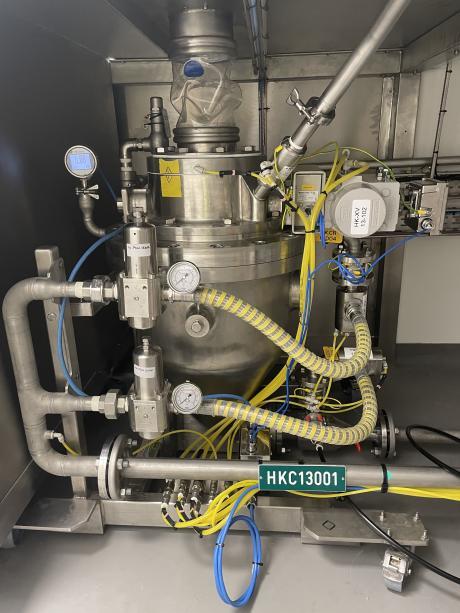 Vista frontal de un componente de transferencia neumática de acero inoxidable, con manómetros, reguladores y tubos flexibles amarillos para el transporte de polvos o gránulos.