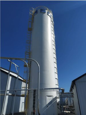 Silo rígido industrial blanco instalado en exterior, equipado con una escalera y una barandilla amarillas bajo un cielo azul claro.